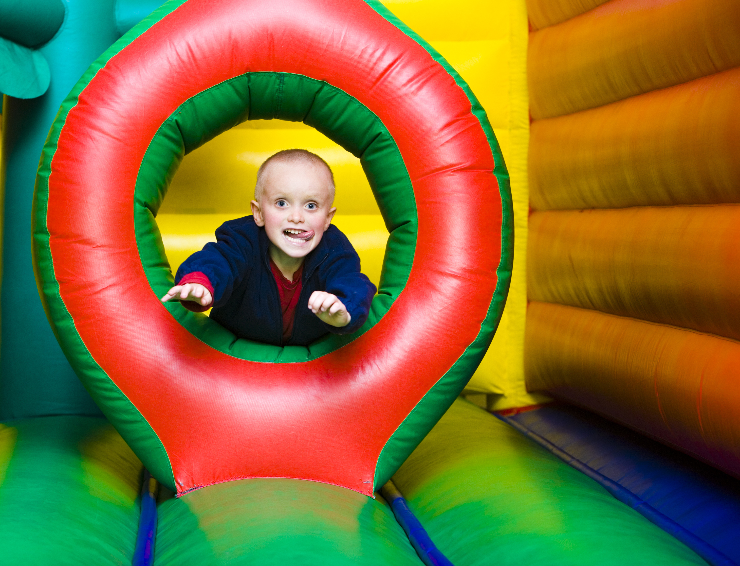 Child having fun climbing through a colorful tunnel in a bounce house rental in Easley, SC, with their tongue sticking out in excitement.