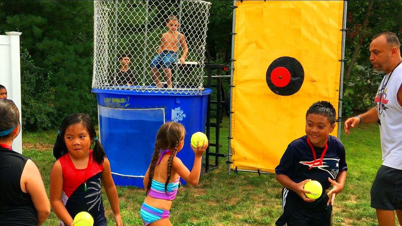 This dunk tank rental in Parker, SC is set up for a lively outdoor summer event with children lined up to take their turn throwing softballs at the bright yellow target. The blue tank features a secure safety cage and clear viewing window, making it a safe and exciting attraction for all ages. Perfect for summer camps, school field days, church picnics, and community festivals in Parker, a dunk tank rental brings energy, laughter, and friendly competition to any event.