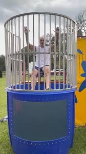 This dunk tank rental in Wade Hampton, SC is set up outdoors on grass, featuring a blue water tank with a clear viewing window and enclosed safety cage above. A participant sits ready above the tank, waiting for the target to be hit. Ideal for school field days, church fundraisers, corporate picnics, and neighborhood events in Wade Hampton, this classic dunk tank rental adds interactive fun and crowd engagement to any outdoor gathering.