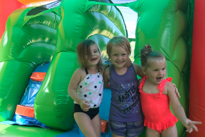 Three young girls laughing and playing inside a green inflatable during a summer water slide rental in Gantt, SC.