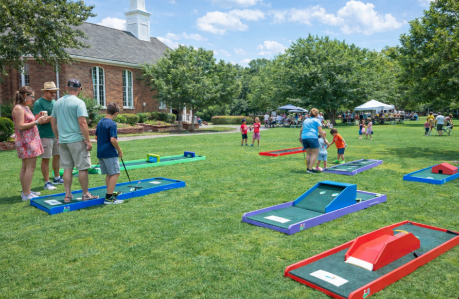 Portable 9-hole mini golf rental setup at a church picnic in Simpsonville, SC with families and kids playing on a sunny day.