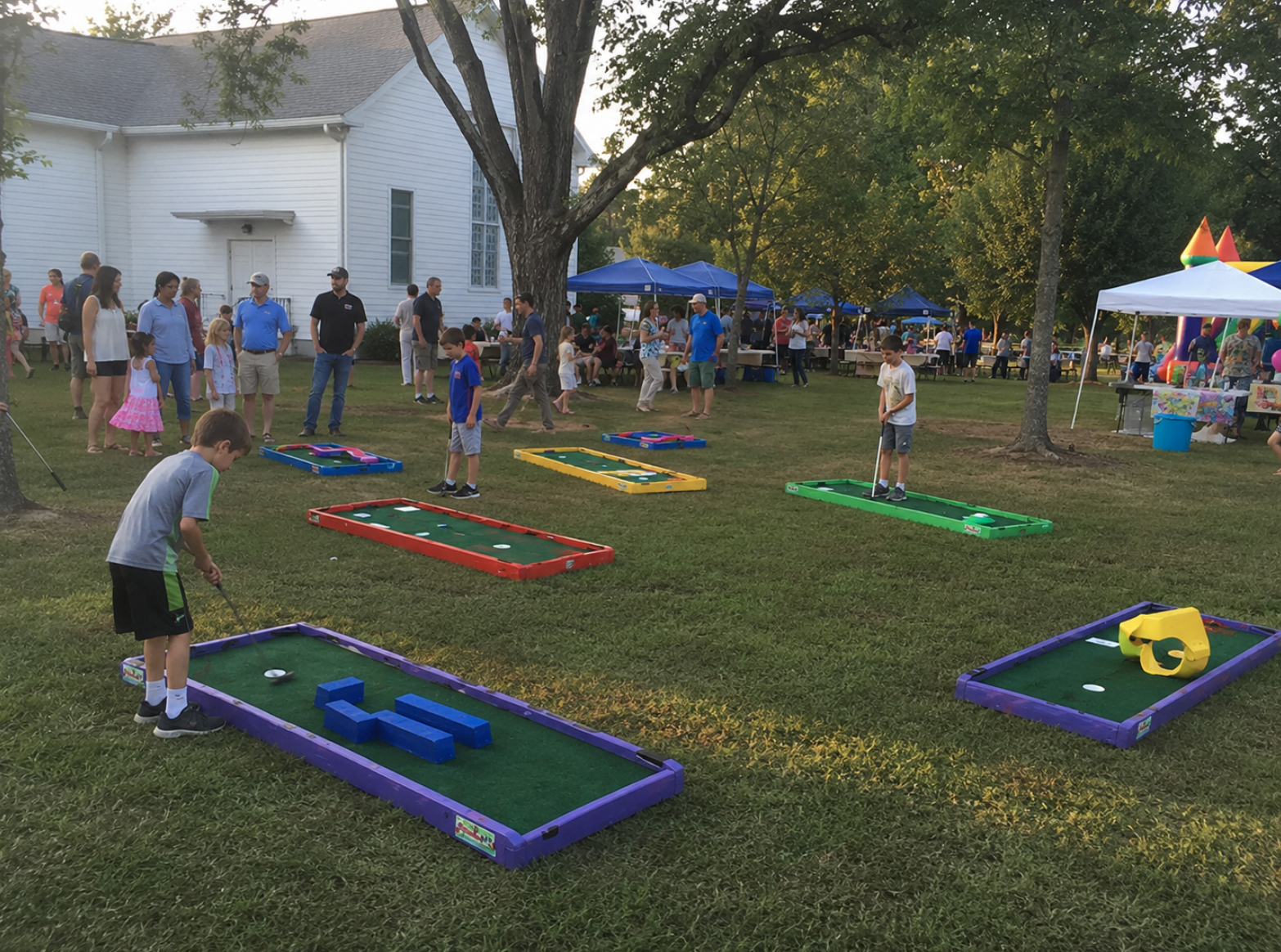 Portable mini golf rentals at a South Carolina community event, with colorful putt-putt lanes arranged on the lawn near a church-style building, pop-up tents, and families gathered together. Children play mini golf while adults socialize in a relaxed outdoor setting.