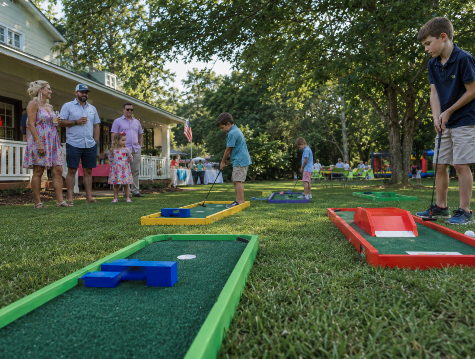 Portable mini golf rentals at a South Carolina family gathering, with colorful mini golf lanes set up across a grassy yard while children play and adults watch nearby. The scene feels like a natural outdoor birthday party with summer light, leafy trees, and a welcoming backyard atmosphere.
