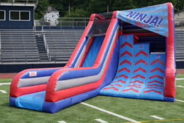 Ninja warrior inflatable obstacle slide with climbing wall, dual lanes, and bright red, blue, and gray colors set up on turf.