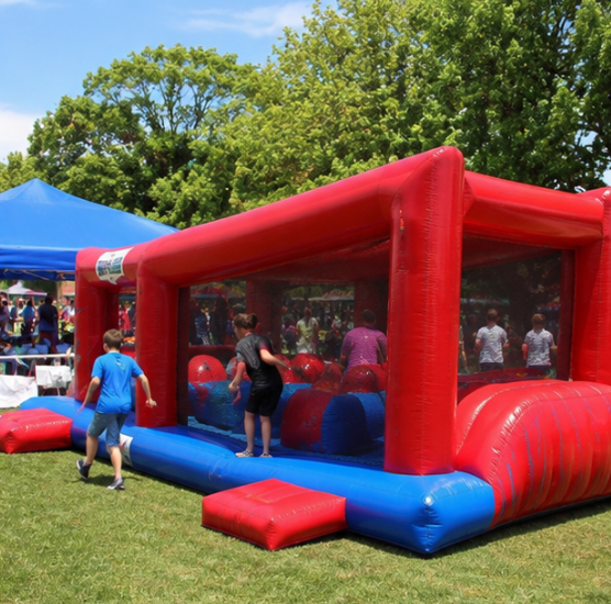 Children running through a red and blue inflatable wipeout-style game on a grassy field during a sunny festival.