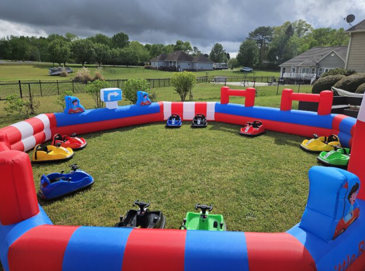 Children riding colorful bumper cars inside a red, blue, and white inflatable arena while other kids watch from the edge.