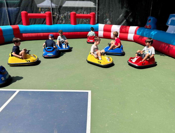 Kids riding blue, red, green, and yellow bumper cars inside a striped inflatable bumper car course.