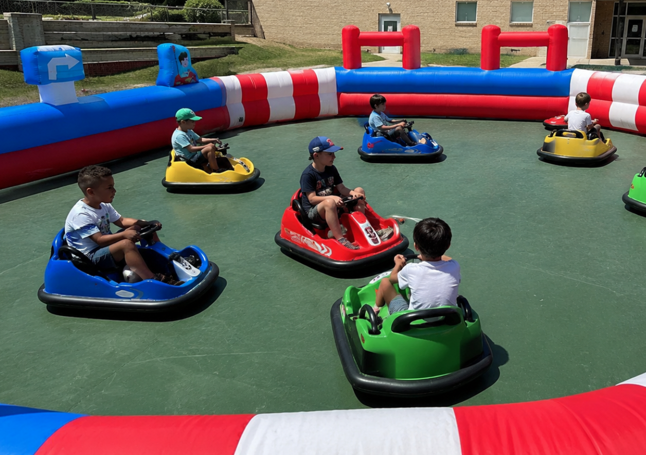 Children driving colorful bumper cars inside a red, blue, and white inflatable bumper car arena.