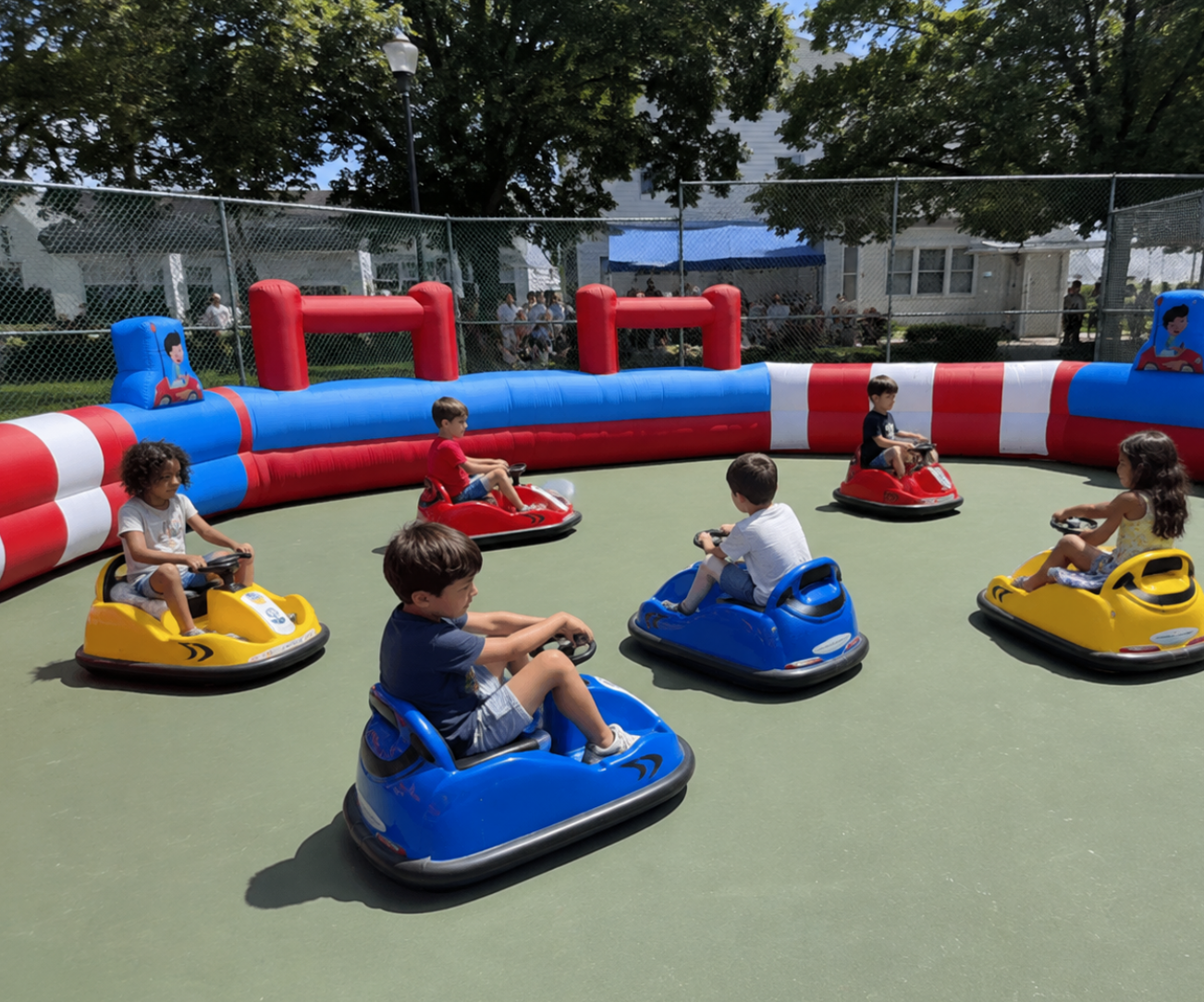 Children riding bumper cars on a smooth play surface inside a red, blue, and white inflatable arena.
