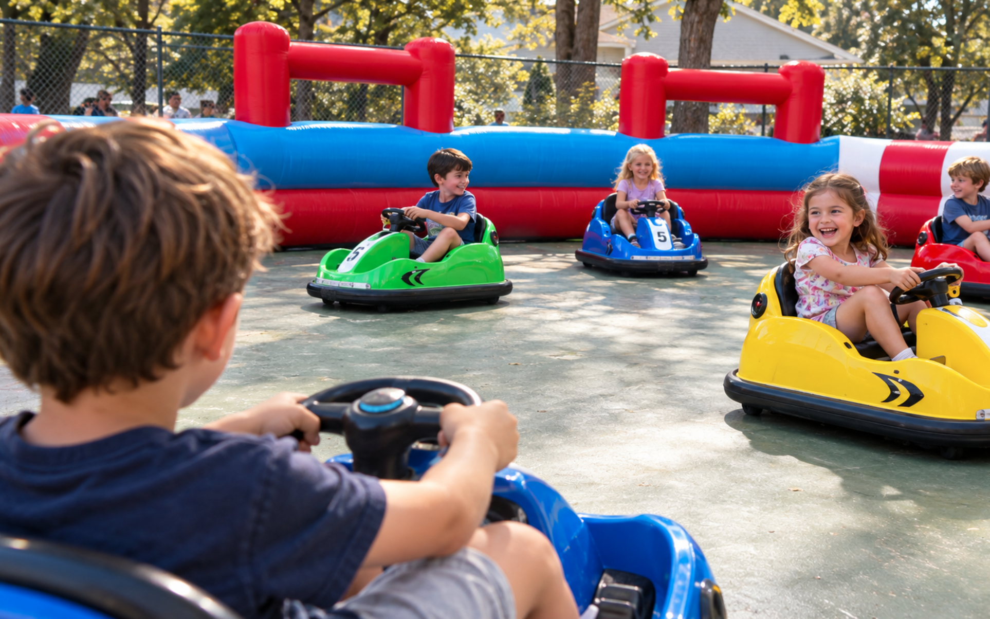 Over-the-shoulder view of a child steering a blue bumper car toward four other children driving colorful cars inside an outdoor inflatable arena.