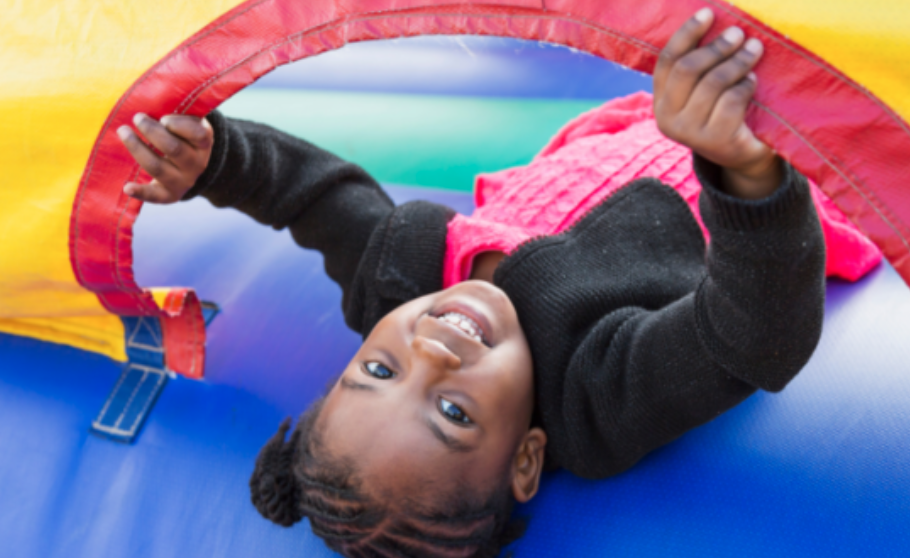 Smiling young girl lying on her back inside a colorful red, yellow, and blue bounce house.