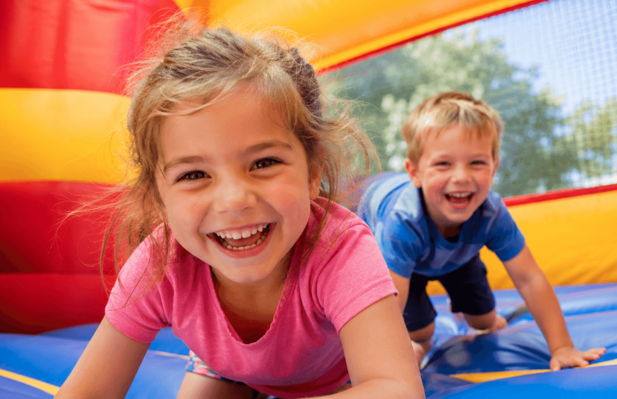 Two smiling children crawling and playing together inside a colorful inflatable bounce house with blue, red, and yellow walls.