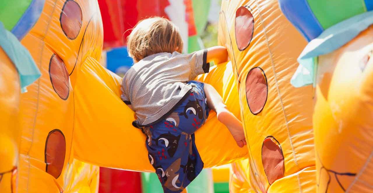 Child climbing inside a colorful inflatable obstacle course at a spring festival, showcasing active entertainment for summer block parties and community events