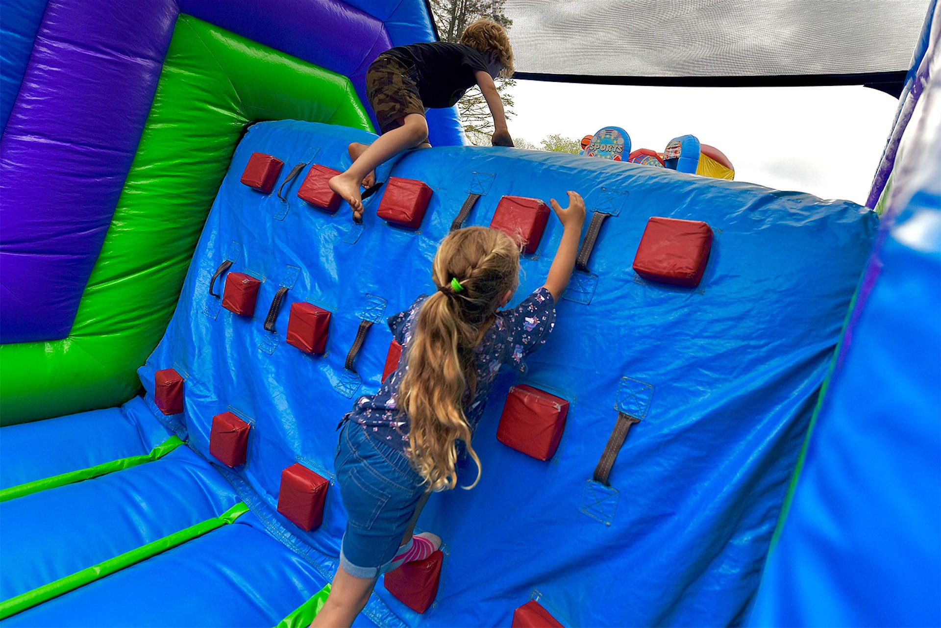 Kids climbing a blue inflatable obstacle course wall at an event in Gantt, SC, featuring padded grips, bright colors, and safe play surfaces.