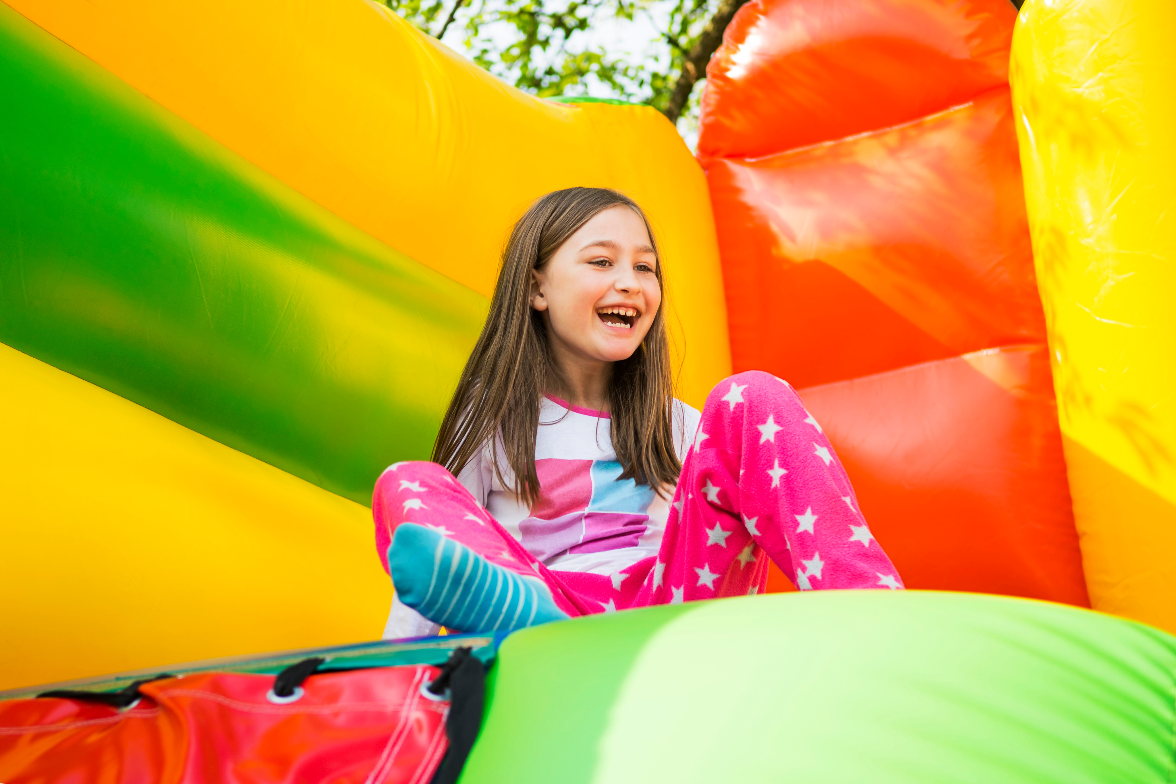 Girl smiling while sliding down a colorful inflatable bounce house at a Greenville, SC party.