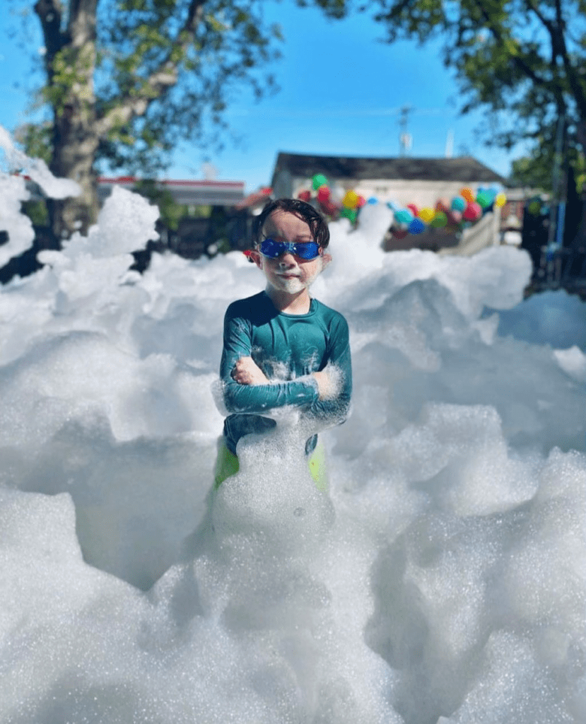 Young boy laughing and playing in deep foam produced by a foam machine at a Fountain Inn SC backyard foam party.
