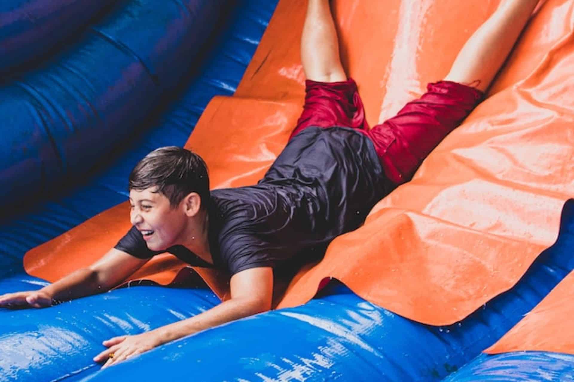 Smiling boy slides down an inflatable water slide during a summer party in Easley, SC.