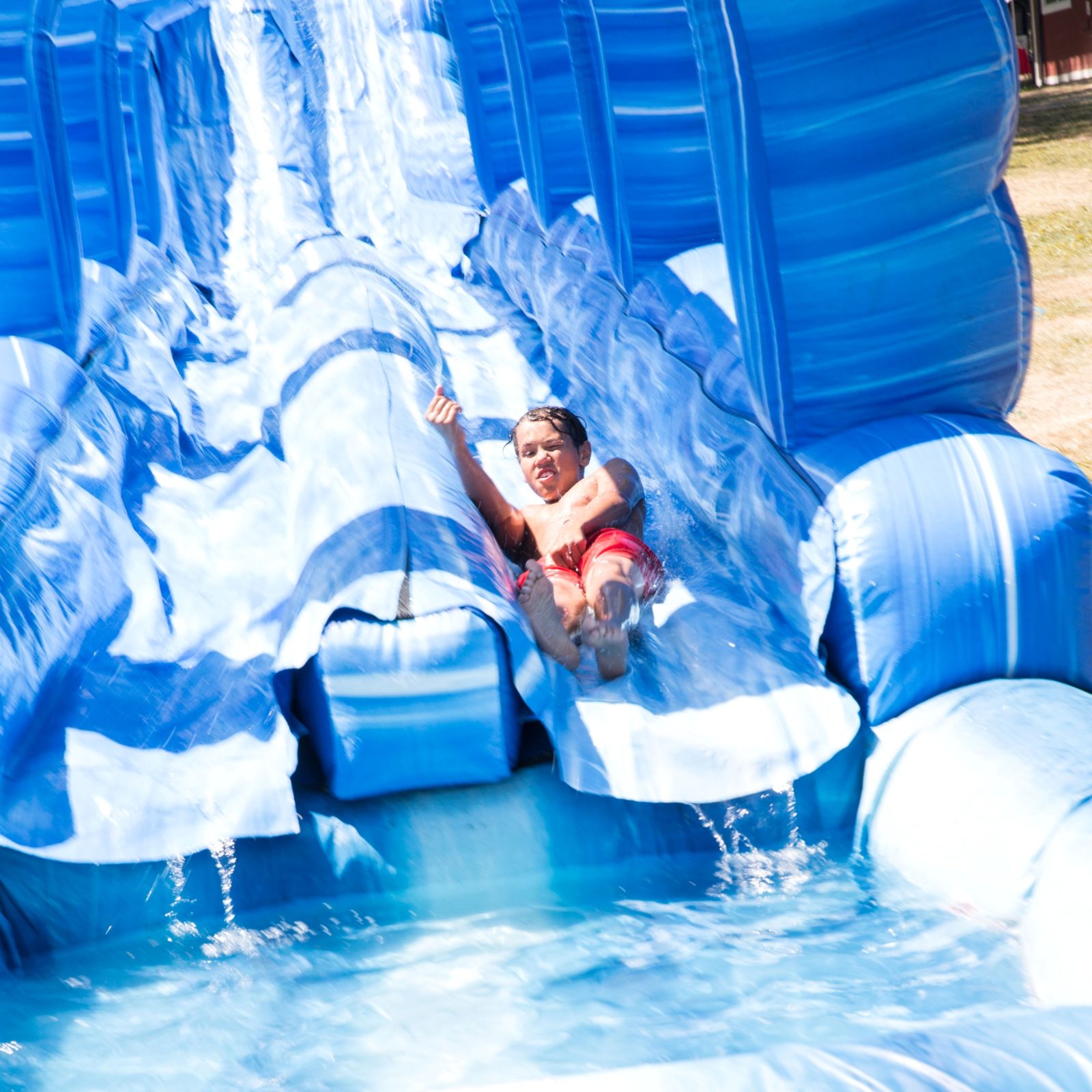 Child splashing into a pool at the bottom of a blue inflatable slide from water slide rentals in Mauldin, SC. Child splashing into a pool at the bottom of a blue inflatable slide from water slide rentals in Mauldin, SC.
