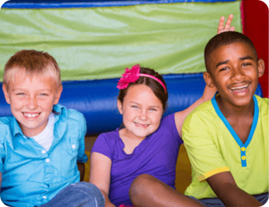 Three happy children sitting inside a colorful inflatable bounce house, smiling and having fun.