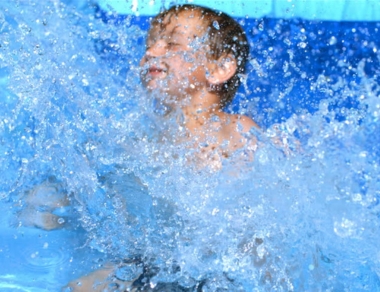 Young boy splashing in the water with a joyful expression, surrounded by blue waves and droplets.