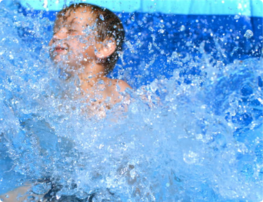 Young boy splashing in the water with a joyful expression, surrounded by blue waves and droplets.