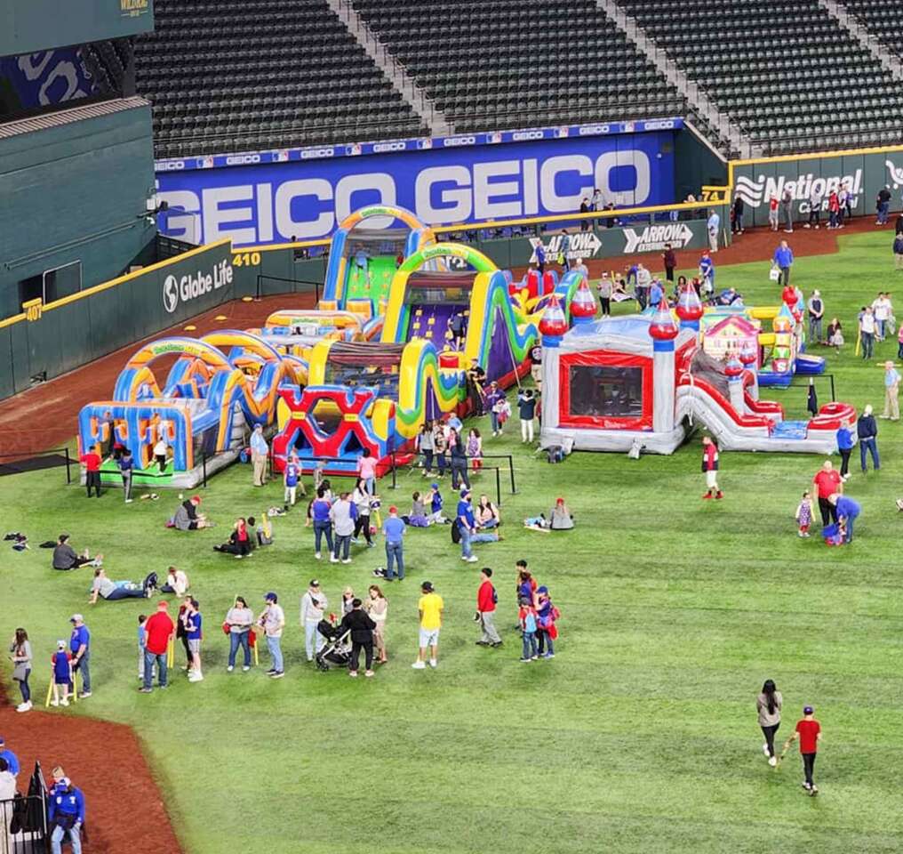  Fort Worth Party Rentals showing a huge event with obstacle courses and and jump houses inside a stadium with hundreds of attendees playing on the fun rentals