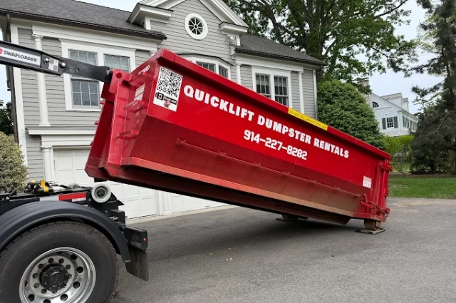 Red roll-off dumpster being delivered in a residential driveway—handled by QuickLift Dumpster Rental