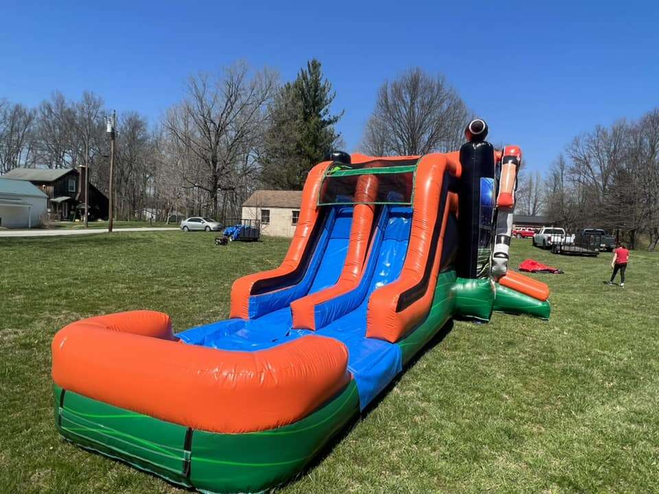 Bright orange, blue, and green inflatable dual-lane water slide on a grassy lawn with children playing on a sunny day.