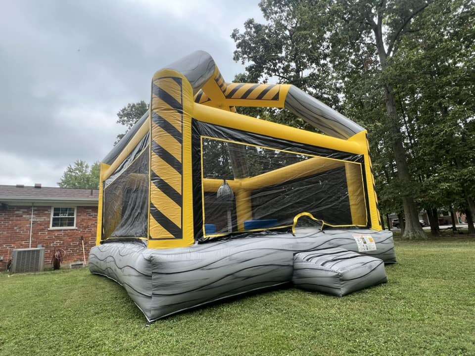 Construction-themed bounce house from Party Go Round with a distinctive yellow and black stripe design, set up on a green lawn in Maineville, OH, perfect for adding a playful work zone vibe to your child's party.