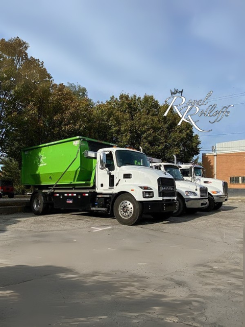 Royal Rolloffs white truck carrying a green dumpster, parked alongside another company truck. Royal Rolloffs white truck carrying a green dumpster, parked alongside another company truck.
