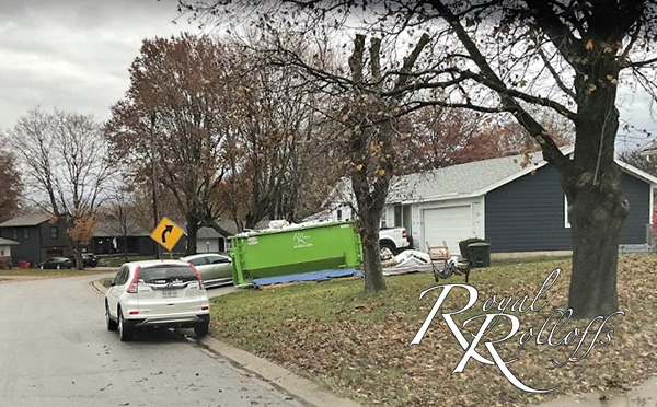 Royal Rolloffs white truck carrying green dumpster to a jobsite
