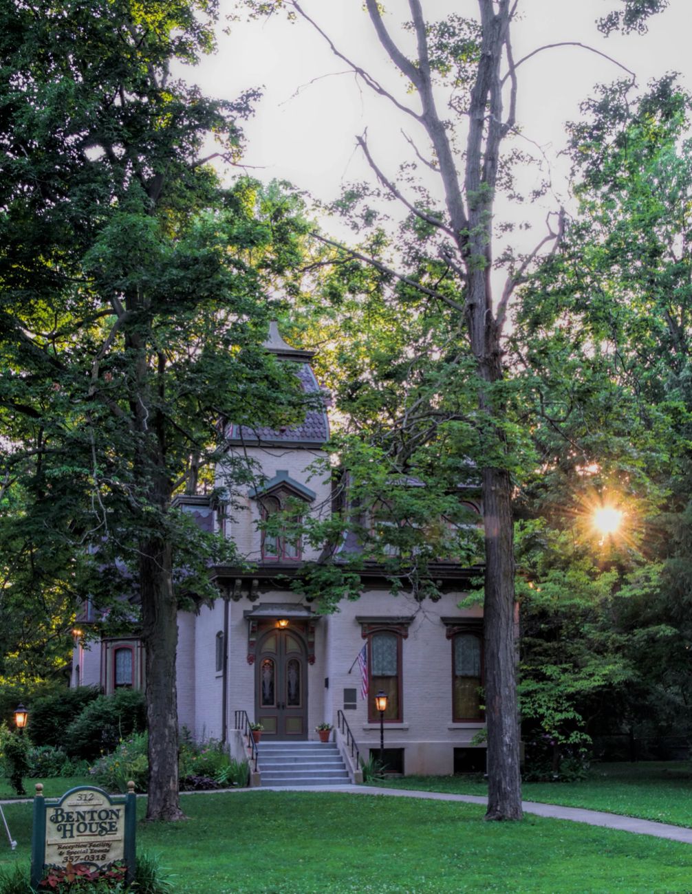 Historic Benton House surrounded by trees at sunset