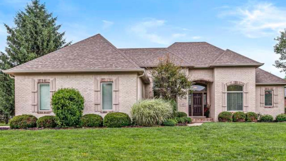Single-story brick home with manicured front lawn and shrubs