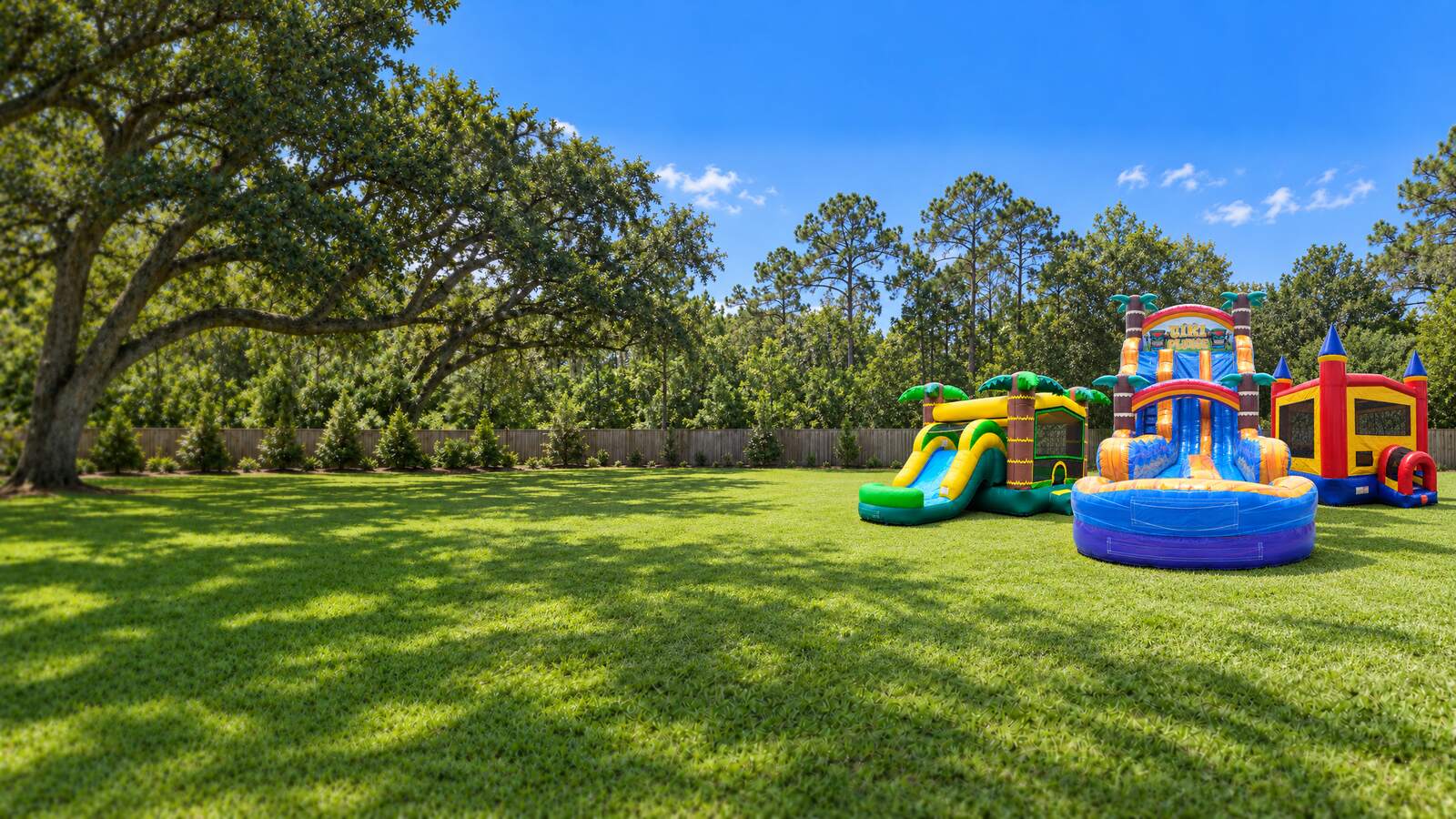 A tropical bounce house combo, a tall double lane water slide and a castle bounce house set up on a green lawn