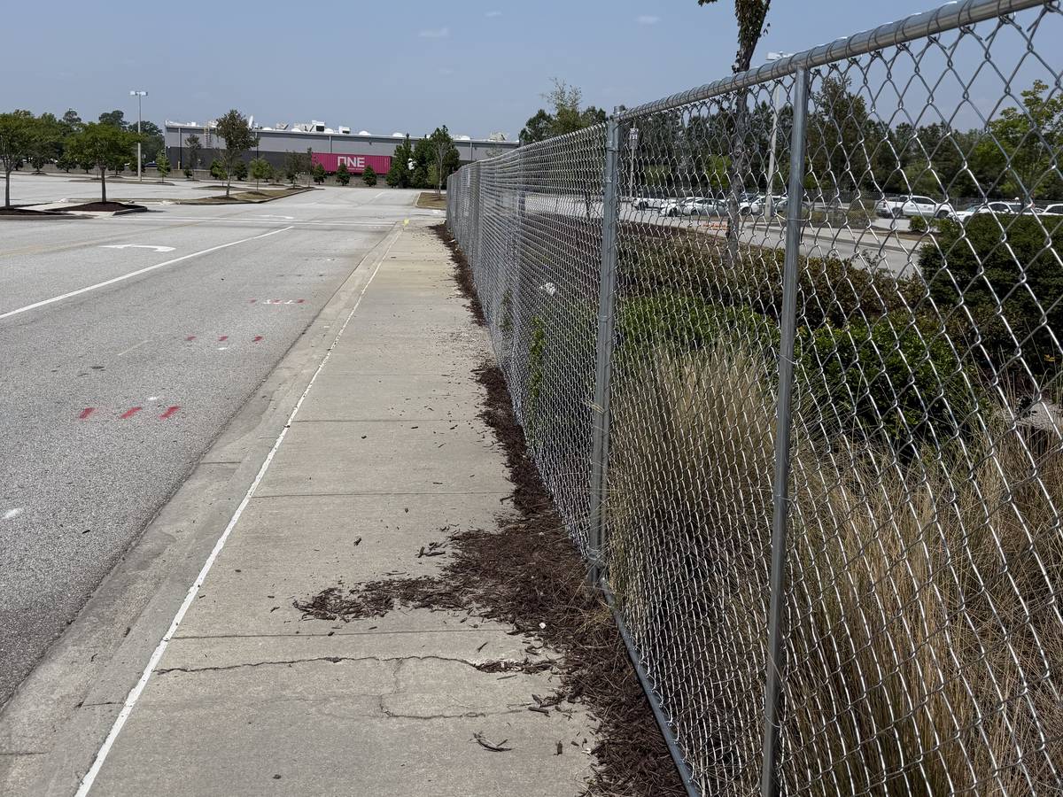 A run of post-driven chainlink fencing along a sidewalk at a commercial site