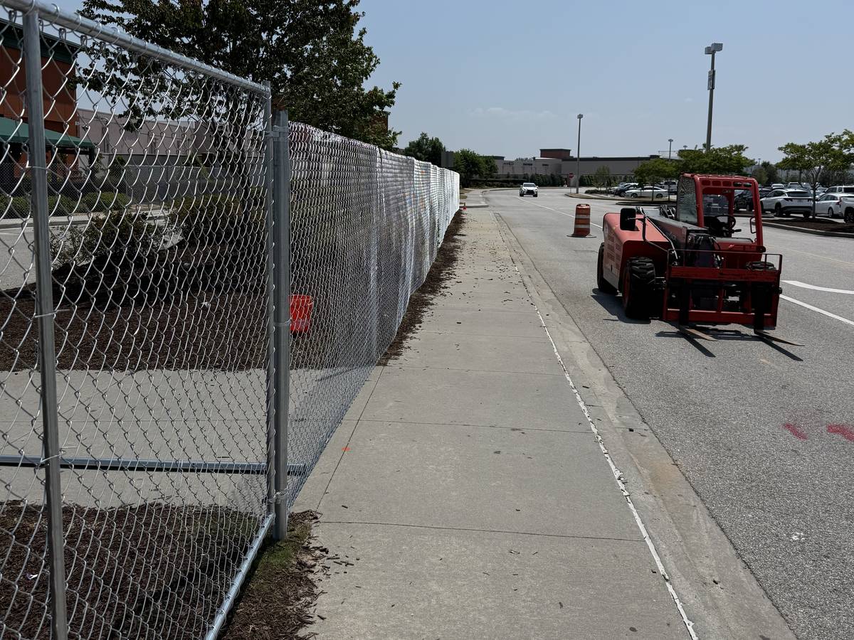 Chainlink fencing with wind screening installed along a commercial street, with a telehandler parked at the curb