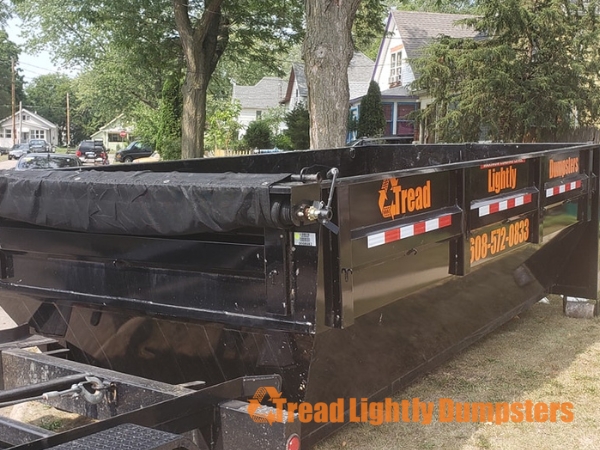 A black dumpster with two doors, displaying the words "Driveway Friendly" in bold orange letters on the top. There are two logos on the sides: one for "FJ Trailers" on the left and another for "ROLLSTER by FJ Trailers" on the right. The bottom of the image features the text "Tread Lightly Dumpsters" in orange.