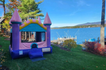 Purple and pink inflatable bounce house castle by Vertical Entertainment House set up by a scenic lakeside.