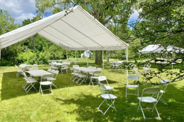 White outdoor canopy tent with folding tables and chairs arranged for an event on a sunny day by Vertical Entertainment.