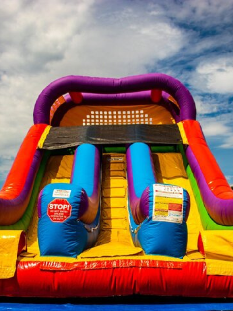 Vertical Entertainment colorful inflatable dual-lane slide under a bright blue sky.