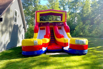 Red, yellow, and blue inflatable double slide by Vertical Entertainment House set up on a sunny lawn.