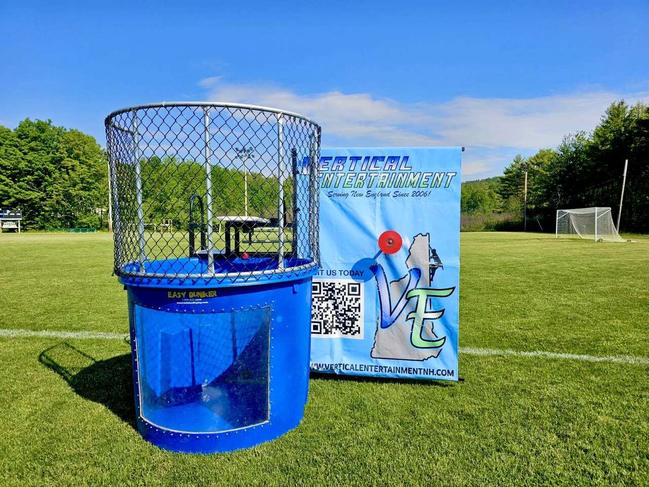 Blue dunk tank attraction by Vertical Entertainment set up on a sports field.
