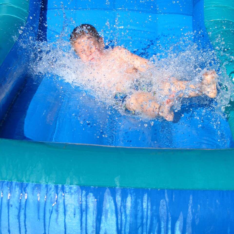 Leader Inflatable Water Slide Rental from We Bring The Party showing a little boy splashing and sliding down a waterslide Leader Inflatable Water Slide Rental from We Bring The Party showing a little boy splashing and sliding down a waterslide