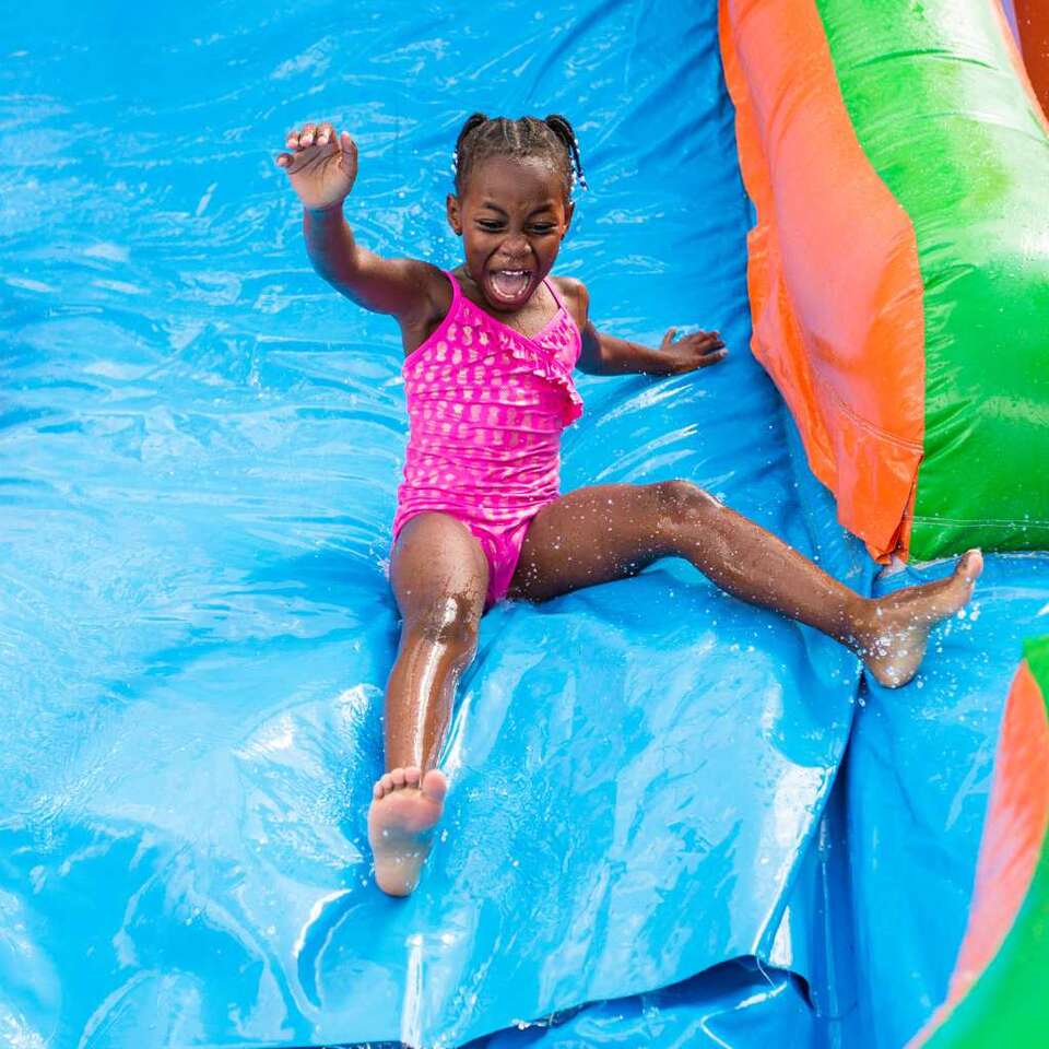 Pflugerville, Tx water slide rentals from We Bring the Party showing a little girl sliding down orange and green water slide Pflugerville, Tx water slide rentals from We Bring the Party showing a little girl sliding down orange and green water slide