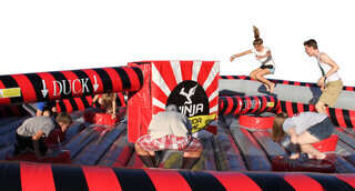 Ninja Warrior-style inflatable game by We Bring the Party with players dodging rotating arms. Ninja Warrior-style inflatable game by We Bring the Party with players dodging rotating arms.