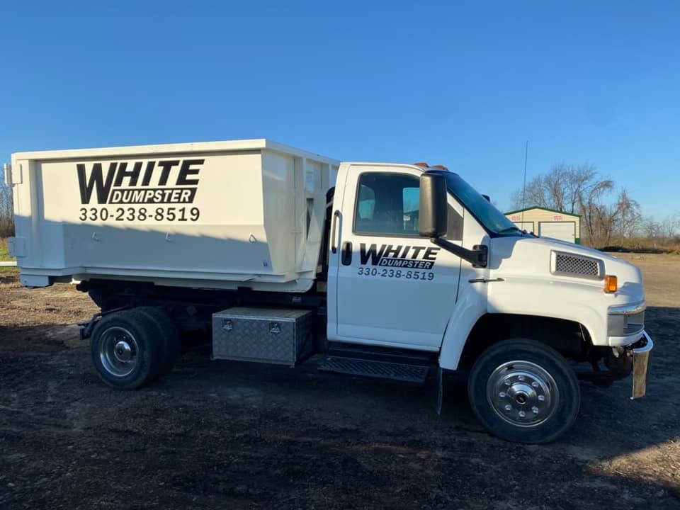 White Dumpster truck with bin parked on dirt lot White Dumpster truck with bin parked on dirt lot